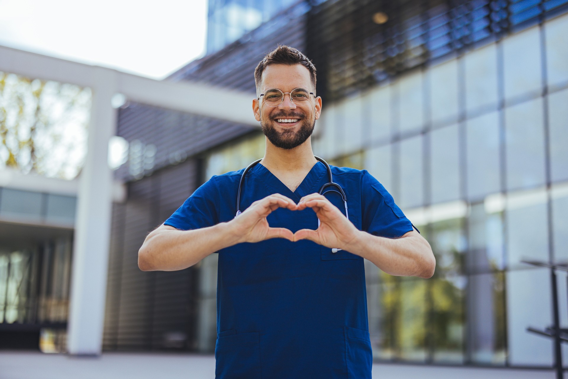 Cheerful male surgeon touching fingers in shape of heart and holding hands near chest.