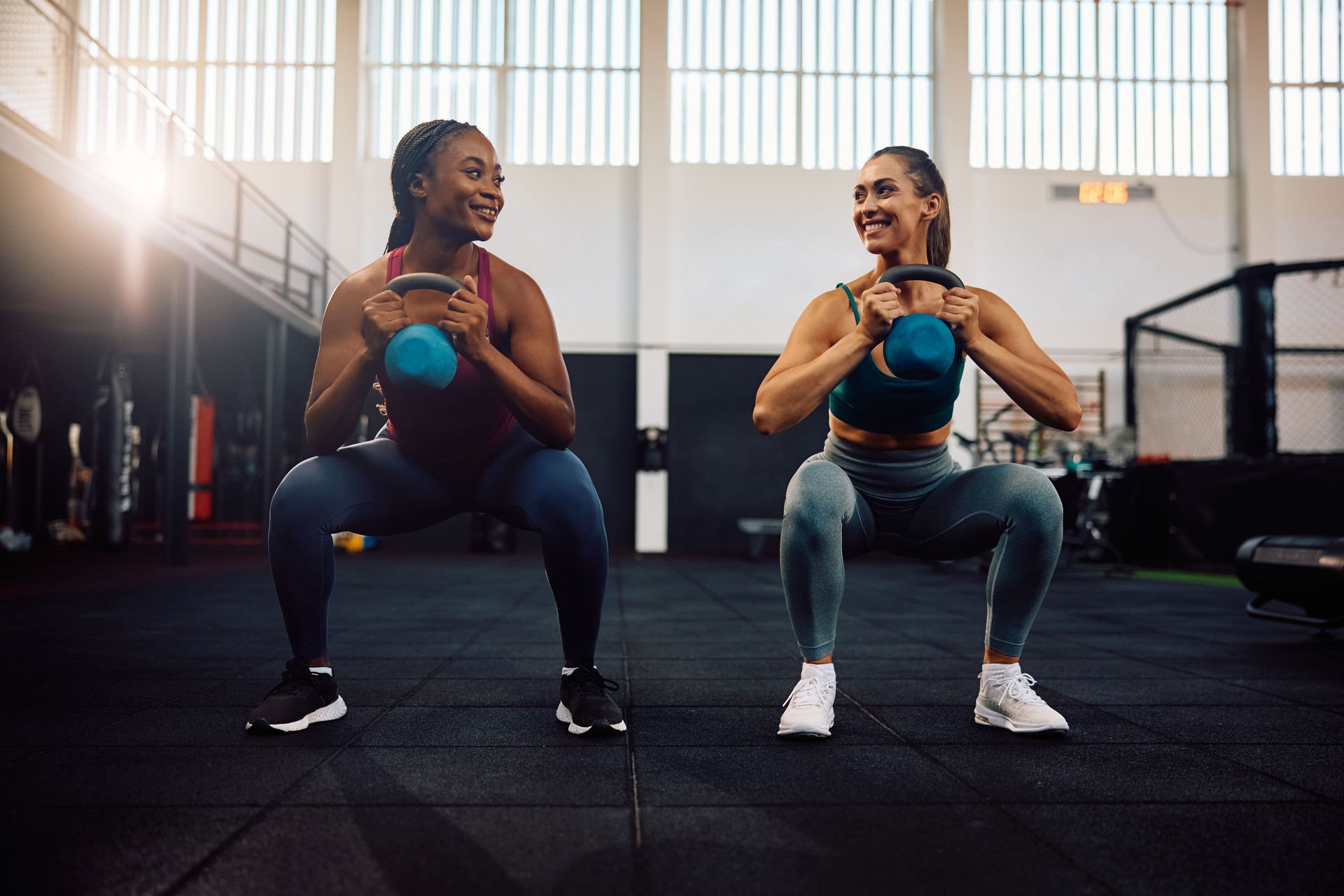 Happy athletic women exercising with kettle bells during gym workout.